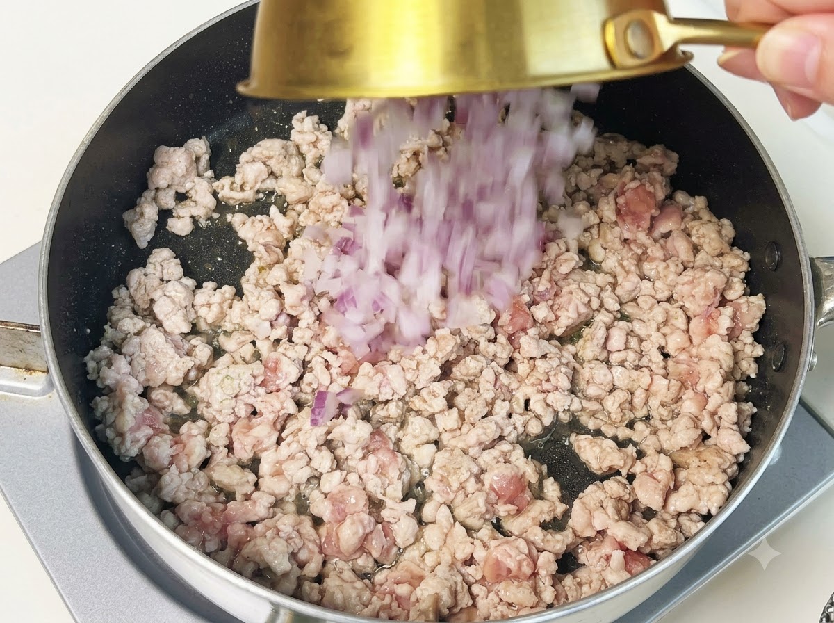 Cipolle viola tritate versate in una padella contenente maiale macinato cotto.