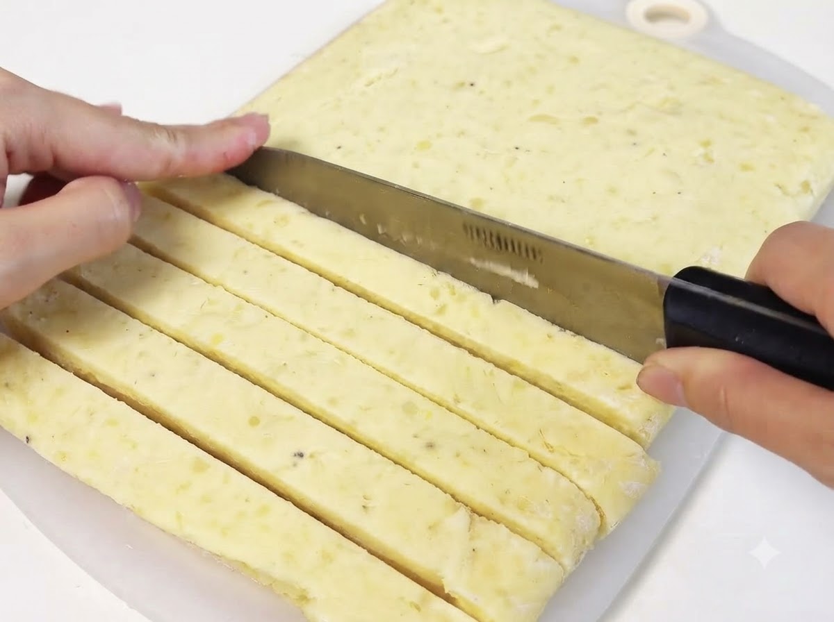 Un coltello che taglia un foglio compatto di purè di patate congelato per ricavare strisce lunghe.