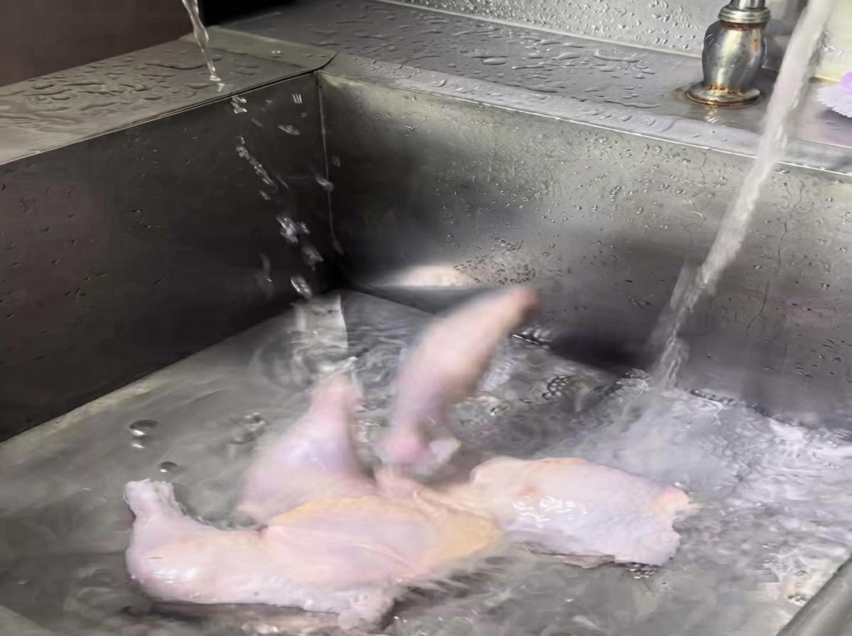 Intere cosce di pollo crude lavate sotto lacqua corrente in un lavandino di acciaio inossidabile.