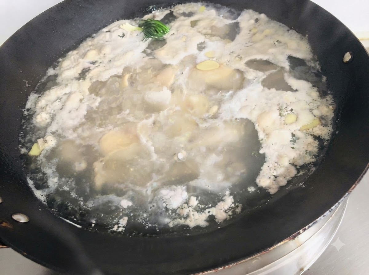 Schiuma e residui che galleggiano sopra lacqua bollente e gli aromi in un grande wok.