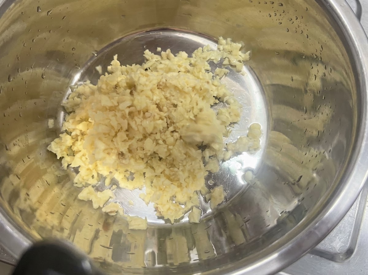 Aglio tritato finemente adagiato in una ciotola di miscelazione in acciaio inossidabile.