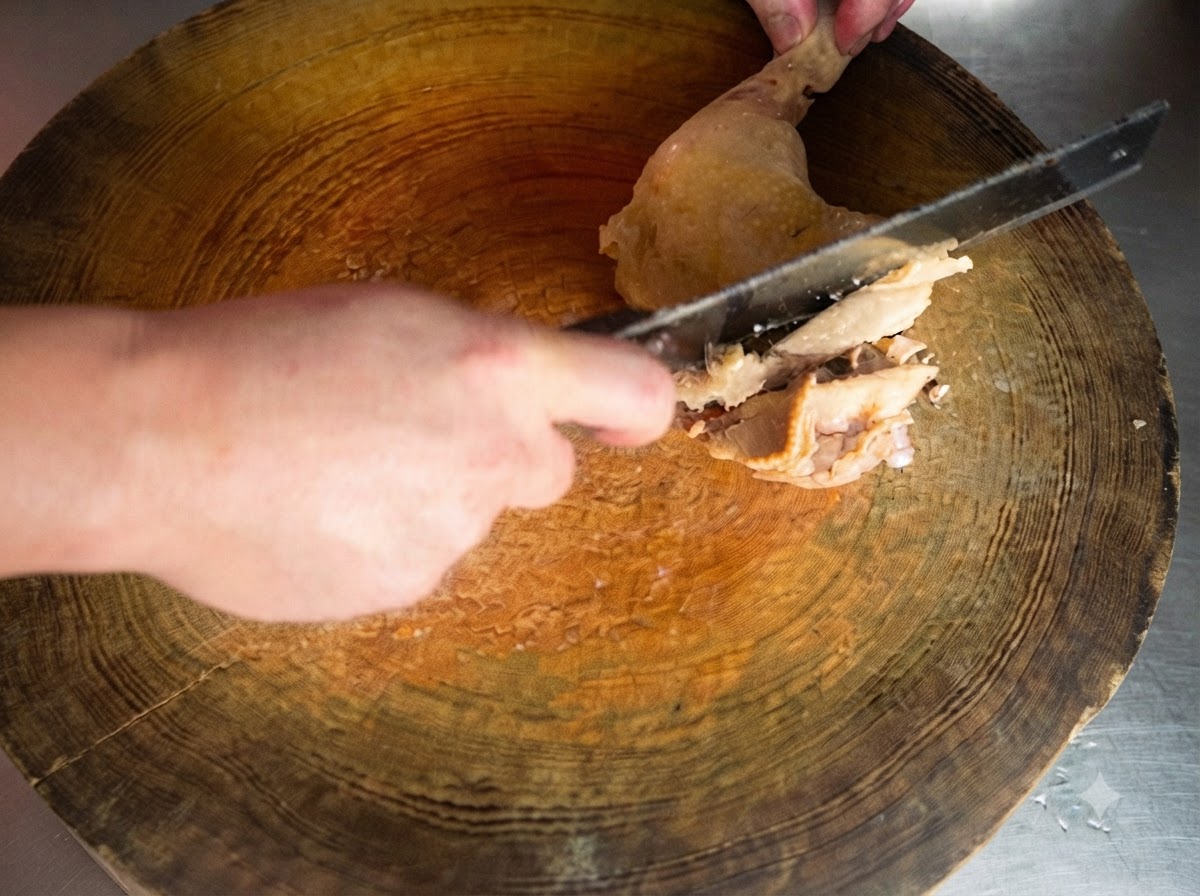 Una mannaia affilata che taglia una coscia di pollo cotta su un tagliere di legno rotondo.
