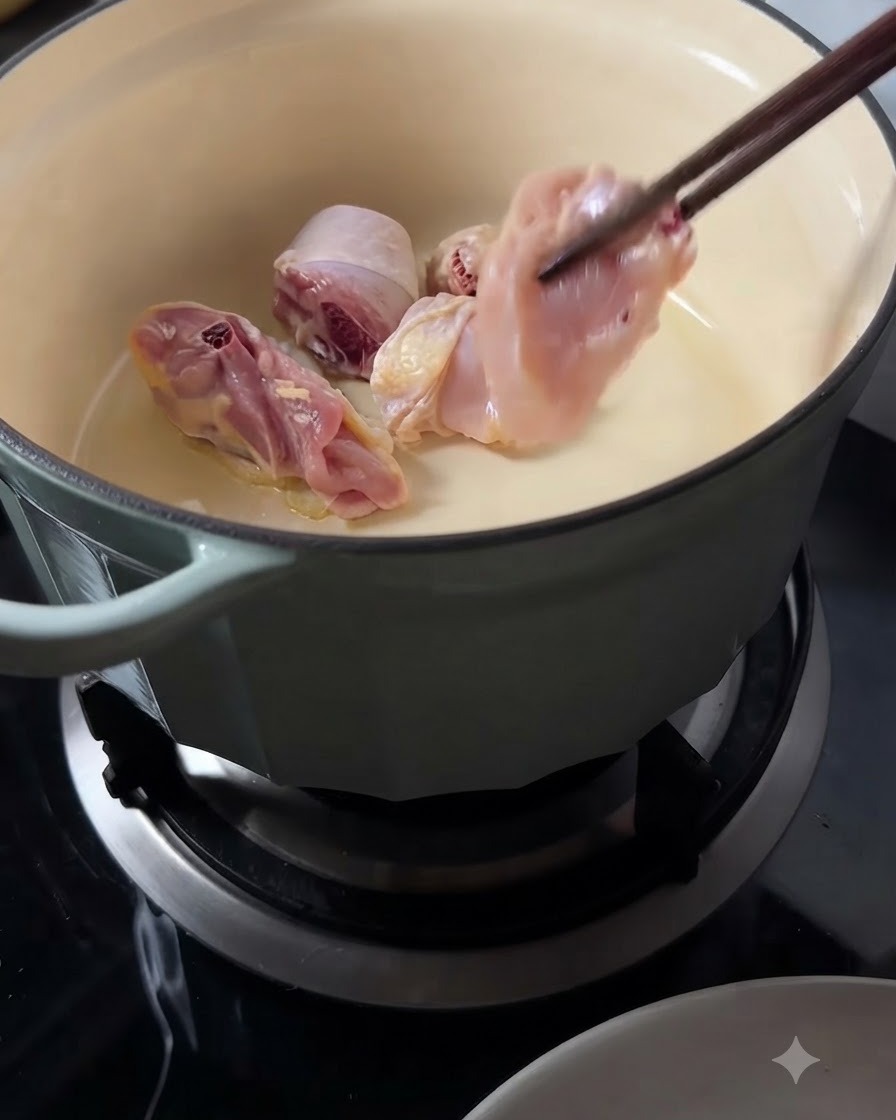 Pezzi di pollo crudo messi in una pentola calda usando lunghe bacchette di legno.