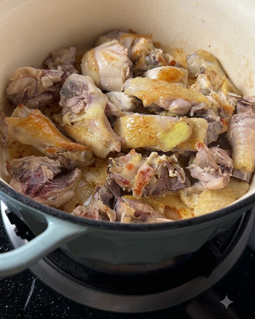 Pezzi di pollo rosolati mescolati con fette di zenzero dorate dentro la pentola.