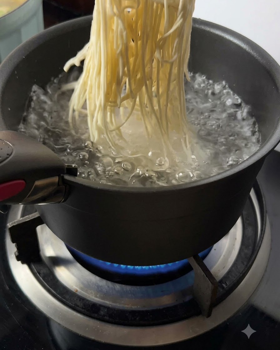 Noodles freschi calati in una pentola di acqua bollente su una fiamma viva.