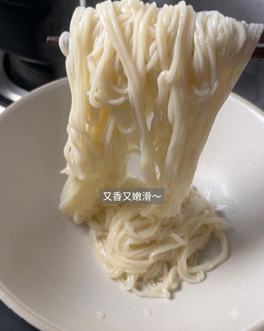 Noodles cotti sollevati con le bacchette e messi in una ciotola da portata bianca vuota.