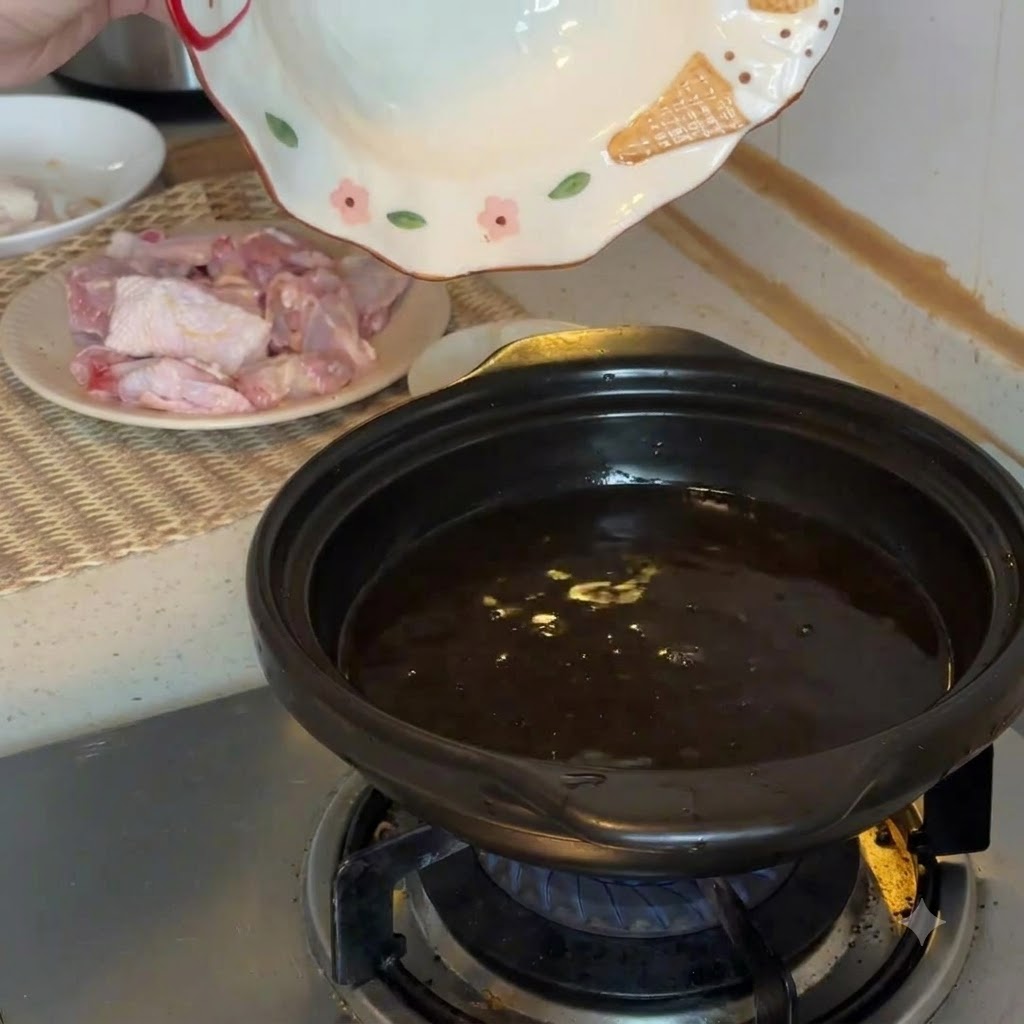 Pezzi di polpa di cocco fresca aggiunti in una pentola di terracotta nera bollente su un fornello a gas.