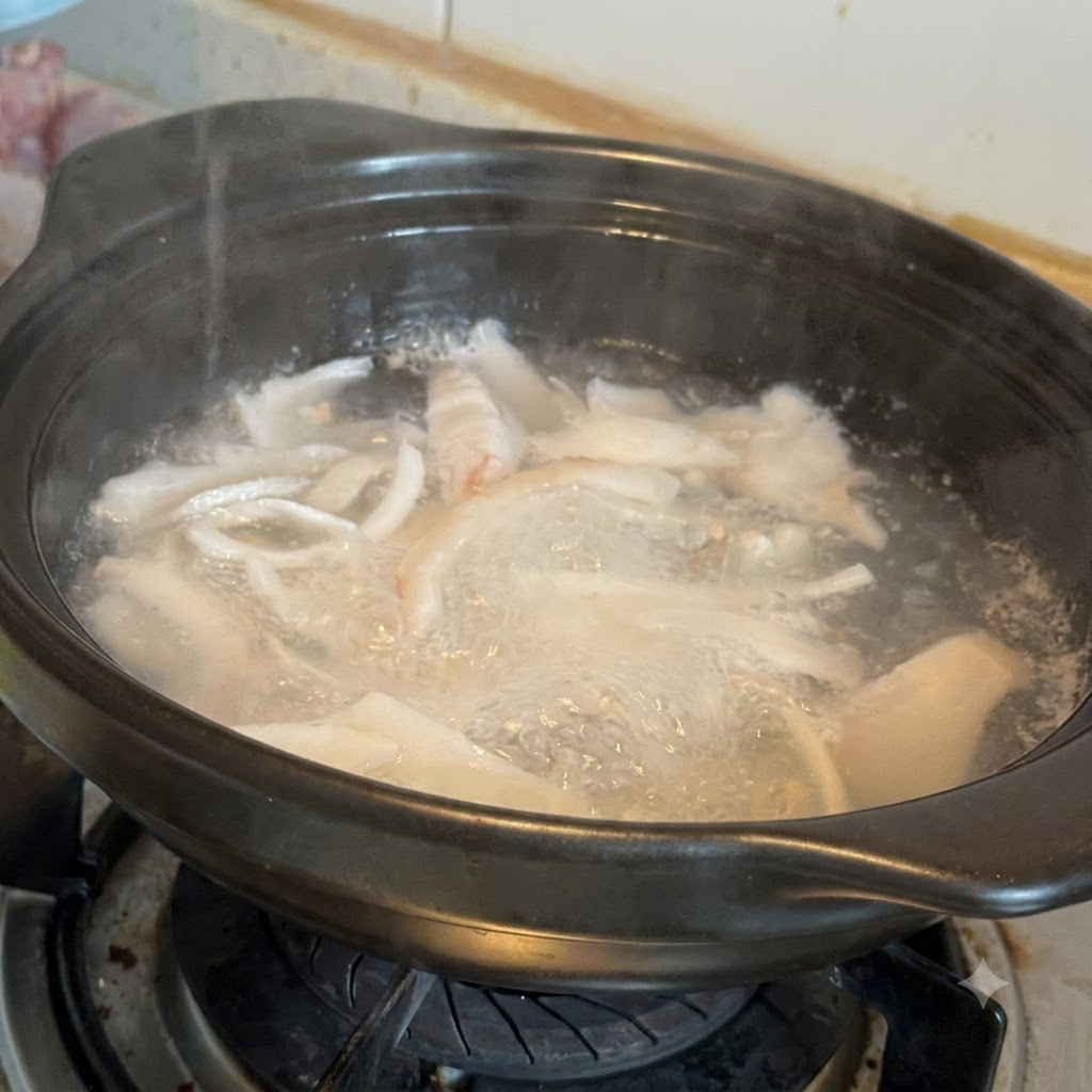 Fette di zenzero, datteri rossi e pezzi di pollo crudo in ebollizione allinterno di una pentola di terracotta nera.