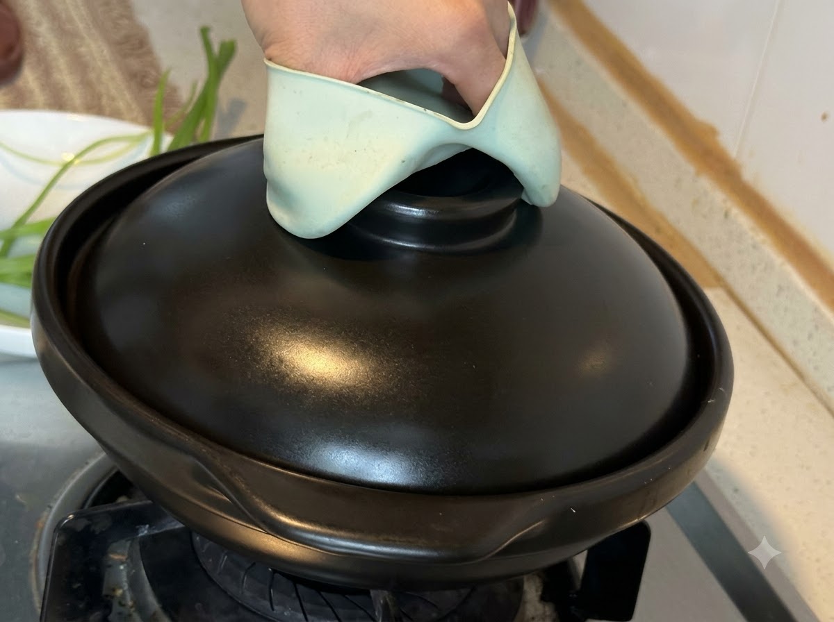 Chiusura del coperchio di una pentola di terracotta nera sul fornello con un supporto in silicone verde.