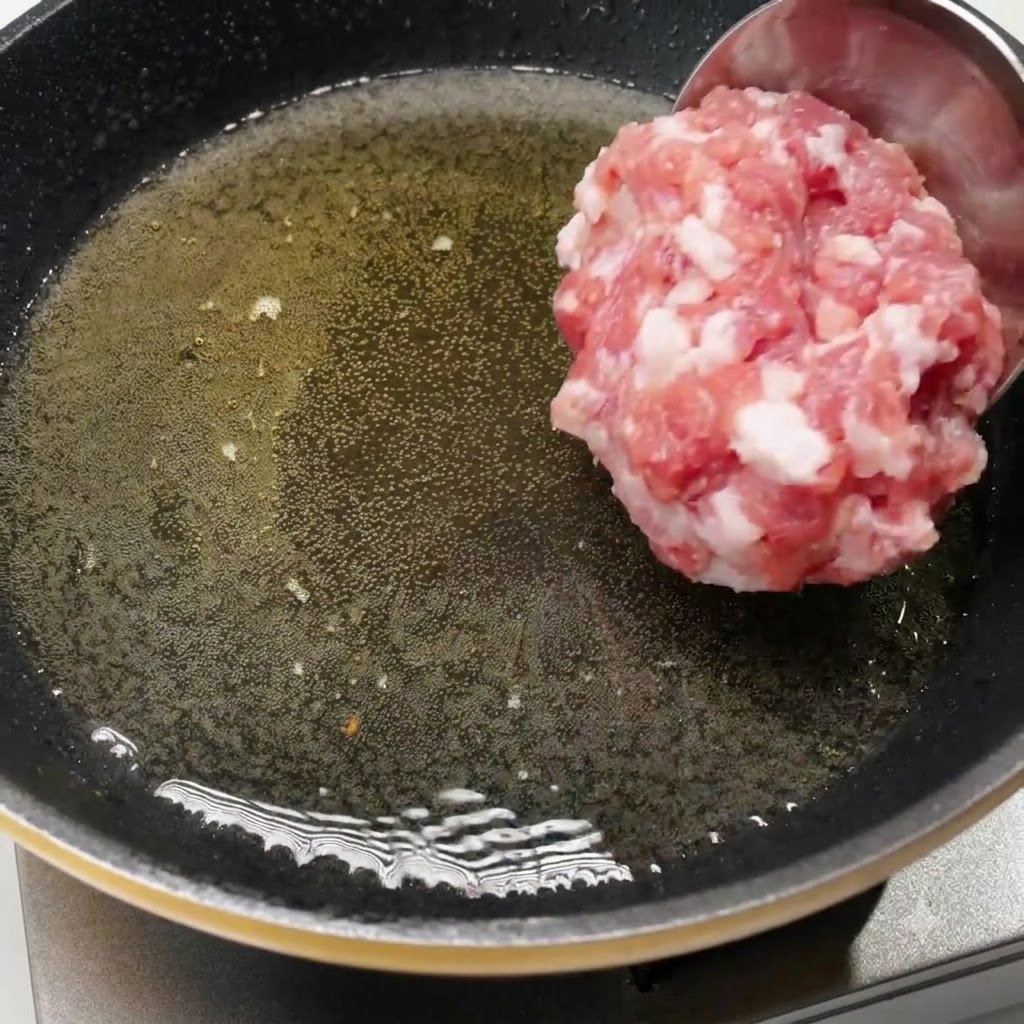 Un mestolo che versa maiale tritato crudo in una padella calda unta dolio.