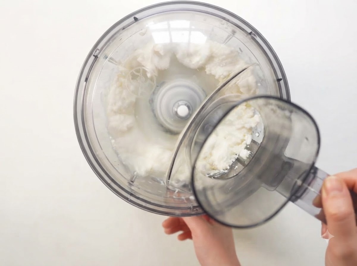 Il robot da cucina in funzione mentre frulla la ricotta e gli ingredienti in un composto bianco e liscio.