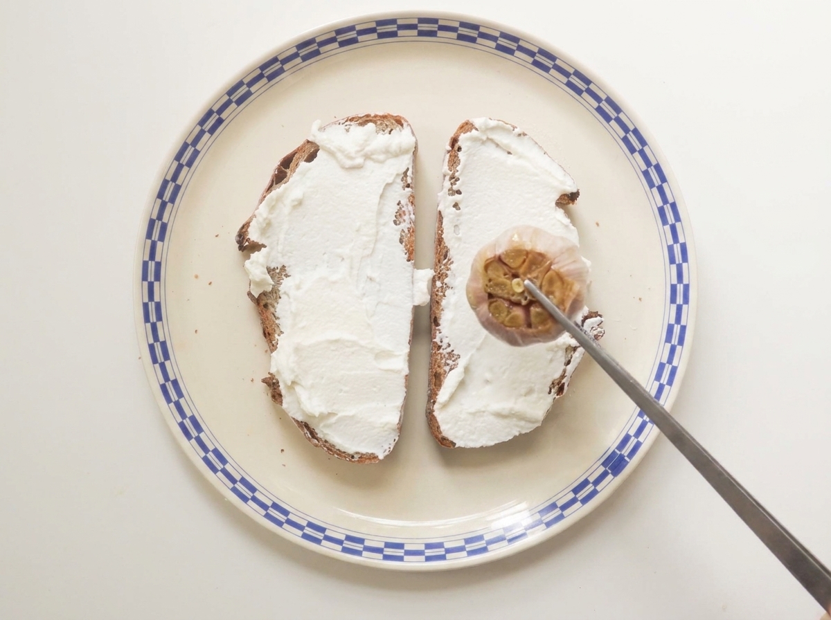 Un bulbo daglio arrosto premuto su del pane a lievitazione naturale spalmato di ricotta su un piatto a motivi.