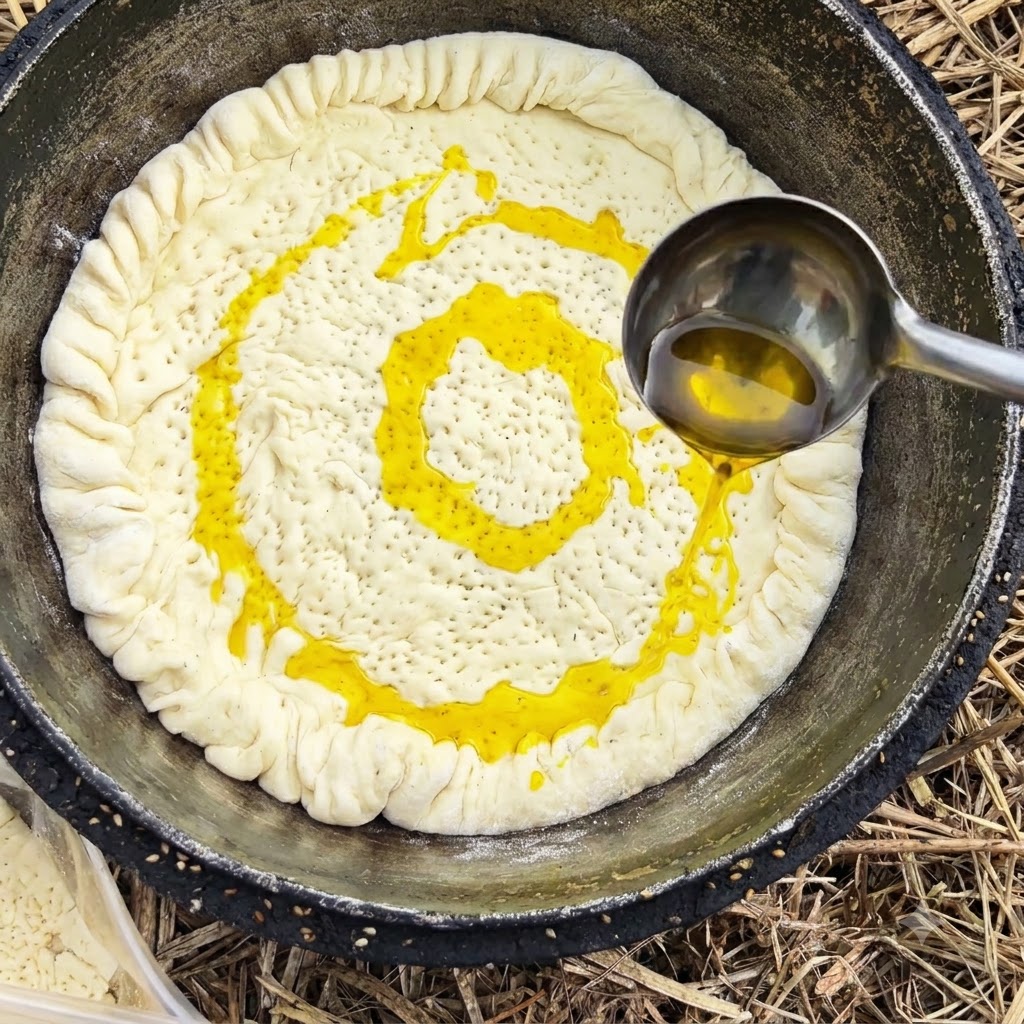 Un mestolo di metallo che versa olio da cucina giallo su una crosta di pasta allinterno di una pentola.