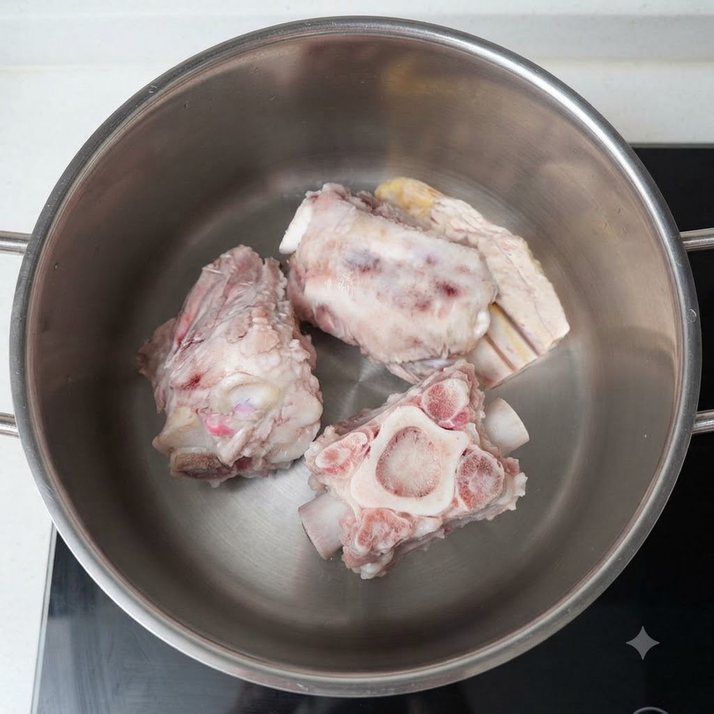 Diverse grosse ossa di maiale con midollo riposano in una pentola di acciaio inossidabile piena dacqua sui fornelli.