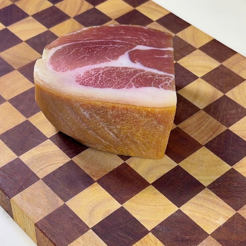 Un pezzo intero di prosciutto stagionato di Xuanwei posizionato su un tagliere di legno a scacchi.